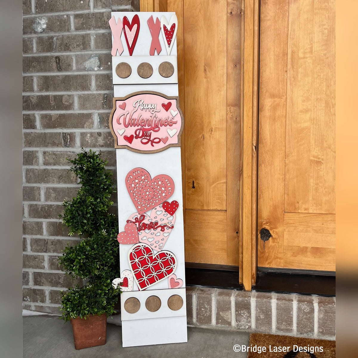 Happy Valentine's Day interchangeable porch leaner with XOXO letters, a Valentine's Day sign, and stacked pink and red hearts on a white wood base