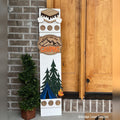 Camping interchangeable porch leaner with a s'mores topper, a mountain camping sign, and pine trees with a tent and campfire on a white wood base