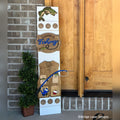 Fishing interchangeable porch leaner with a bass fish, a Fishing sign, and a fishing vest with a rod on a white wood base by a front door