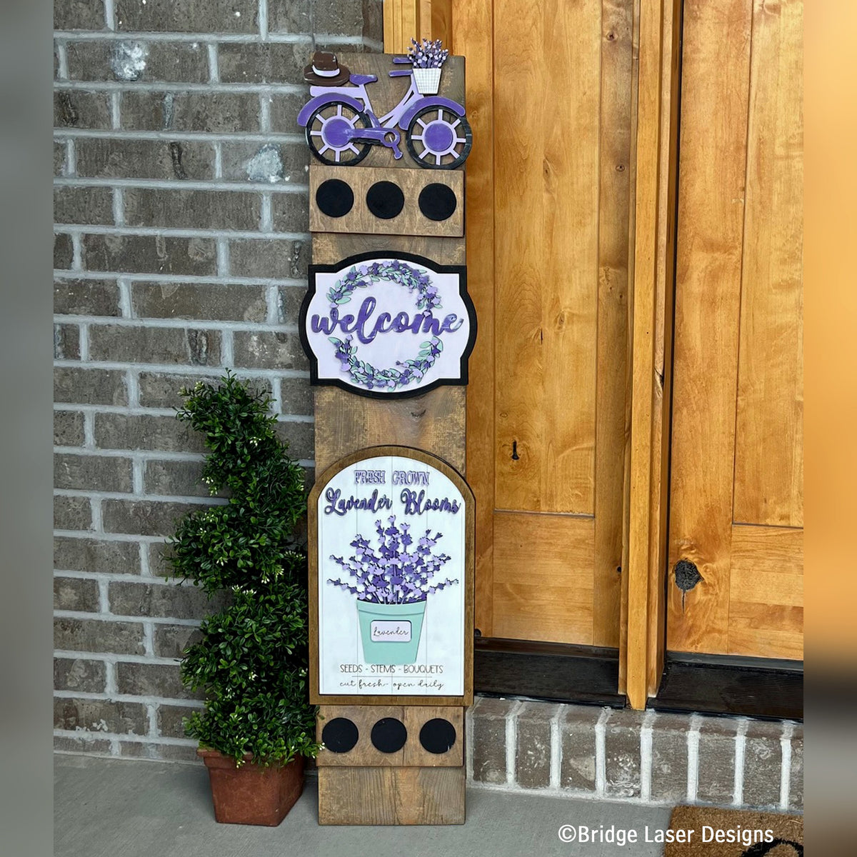Spring lavender interchangeable porch leaner with a bicycle, a lavender Welcome sign, and a Lavender Blooms sign on a stained wood base