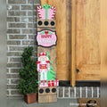 Happy Holidays interchangeable porch leaner with a gift topper, a pink Happy Holidays sign, and a nutcracker with a tree on a stained wood base
