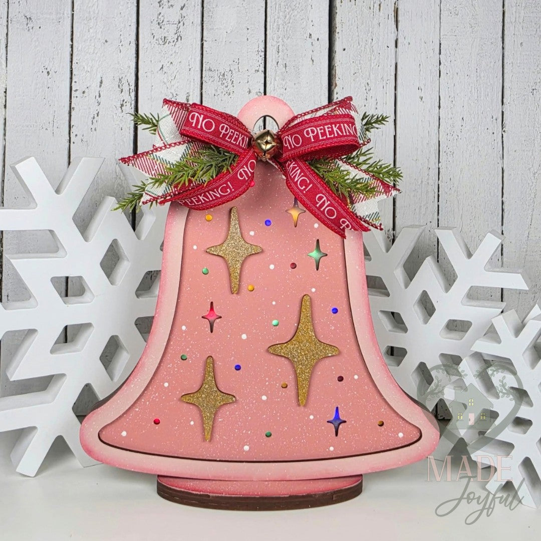 Pink retro light up Christmas bell with gold starbursts and a red ribbon bow on a wood base, hand-painted in Brentwood, TN.