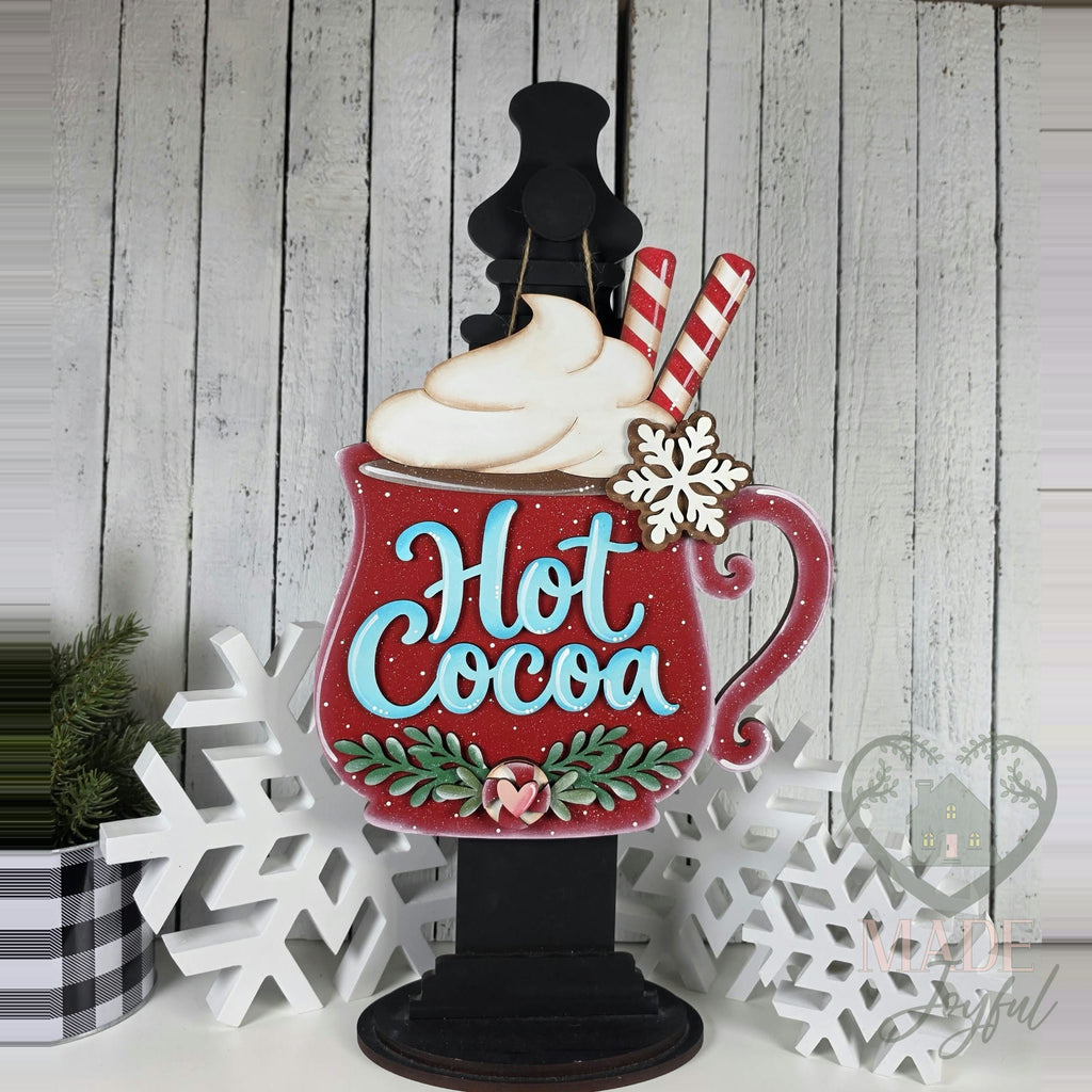 Red Hot Cocoa mug door hanger with whipped cream, peppermint sticks, snowflake, and holly displayed on a black post, hand-painted in Brentwood, TN.